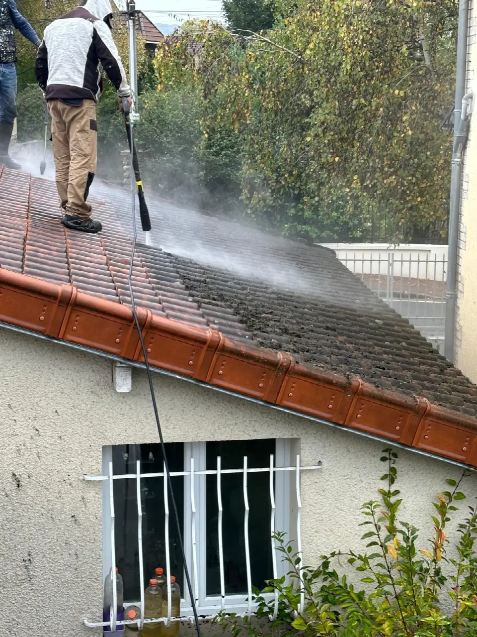 Nettoyage à haute pression d'une toiture en tuiles : la partie nettoyée contraste avec la partie encore couverte de mousse