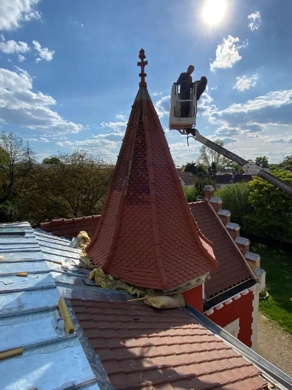 Toit conique d'une tourelle en tuiles écaille, couvreur en nacelle à son sommet et couverture en zinc en cours au premier plan